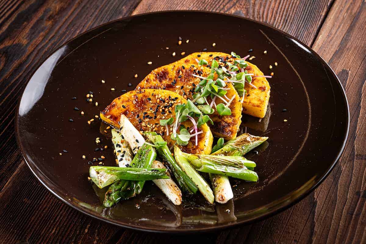 Ein Teller mit Butternusskürbis, Gemüse und Sesamkörnern, serviert auf braunen Teller