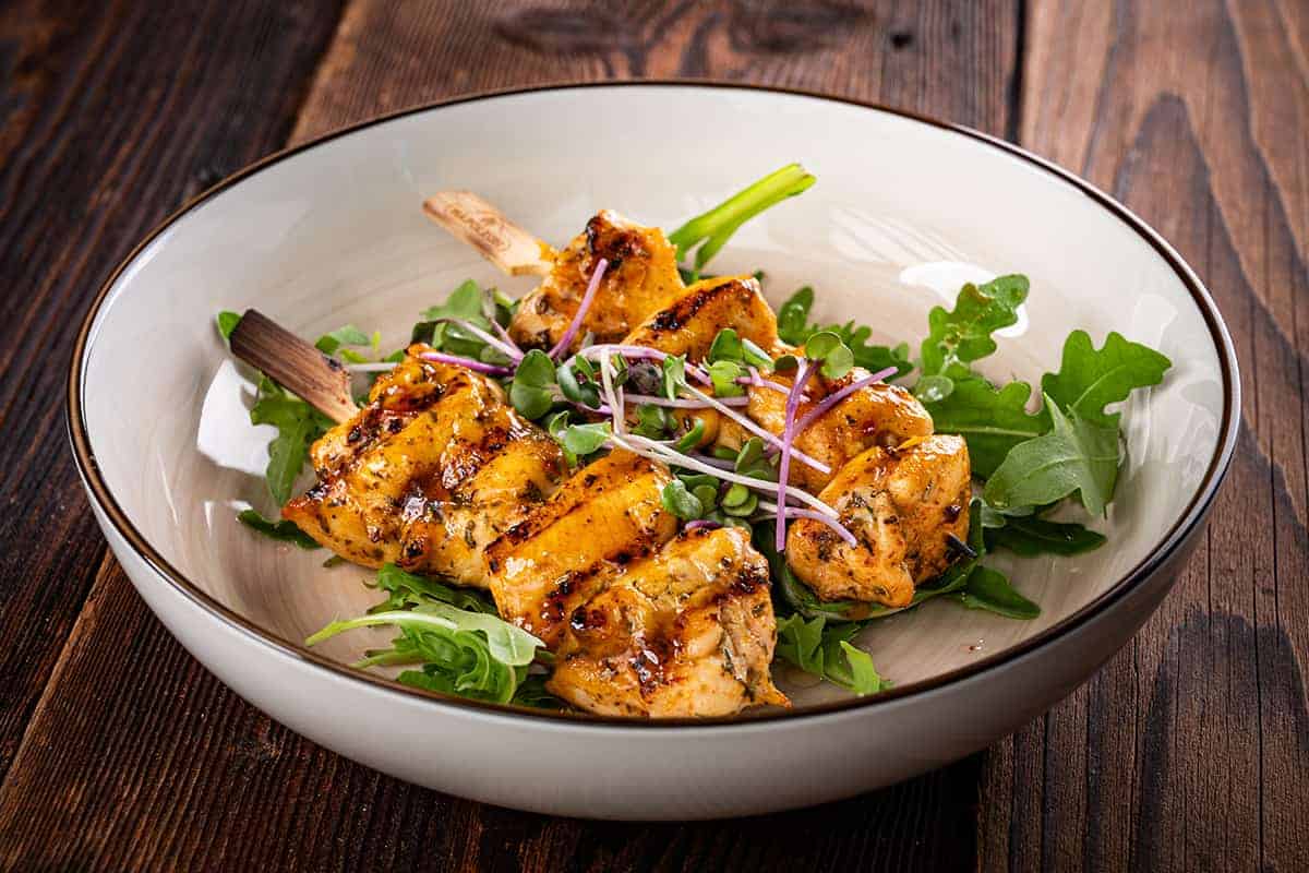 Hendlspieße, serviert im tiefen Teller und garniert mit frischer Rucola und Kresse.