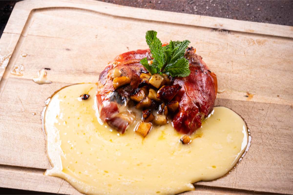 Camembert im Rohschinkenmantel auf einem Brett mit geschmolzenem Käse