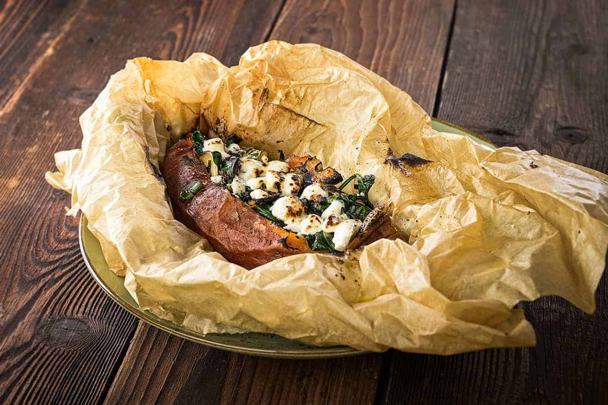 Ein gebackenes Kartoffelgericht mit Feta, in Papier gewickelt, auf einem Holztablett präsentiert