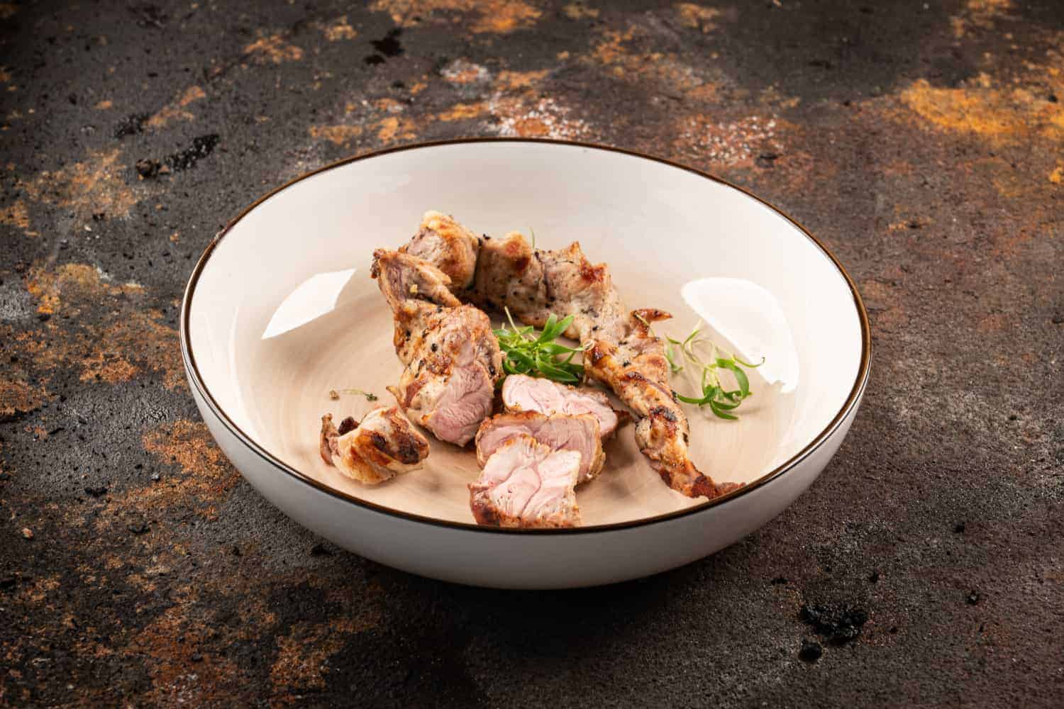 Gegrilltes Lagarto vom Iberico Schwein, in Tranchen geschnitten und in einer weißen Schale mit Kräutern angerichtet.